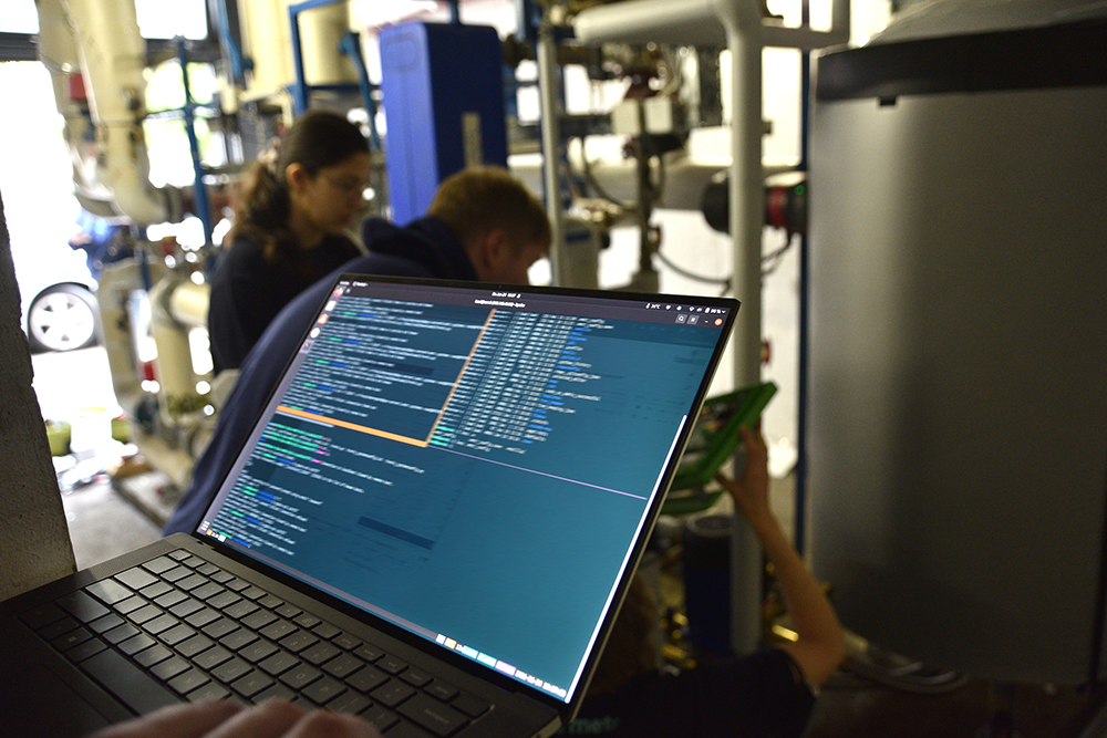 Das Foto zeigt im Vordergrund einen Laptop mit Code und im Hintergrund drei Mitarbeiterinnen und Mitarbeiter von metr bei der Installation der Lösung.